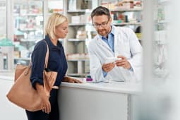 Un pharmacien montre un m&eacute;dicament &agrave; une patiente.