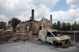 Maison et voiture br&ucirc;l&eacute;es apr&egrave;s un incendie, ruines visibles.