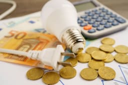 Une calculatrice, une ampoule et des pi&egrave;ces pour symboliser le co&ucirc;t de l'&eacute;lectricit&eacute;.