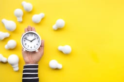 Quelqu'un tient une horloge sur fond jaune avec des ampoules tout autour.