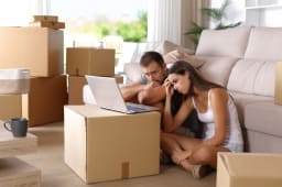 Un homme et une femme l'air inquiet, consultant un ordinateur portable et entourés de cartons de déménagement.
