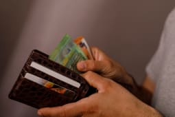 Gros plan des mains d'une personne tenant un portefeuille en cuir marron rempli de billets en euros et de cartes de cr&eacute;dit