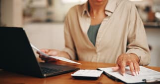 Femme, mains et document dans un appartement avec un ordinateur portable, une calculatrice et une administration pour les factures de services publics. Personne, paperasse et ordinateur &agrave; la maison avec planification financi&egrave;re, d&eacute;penses domestiques et d&eacute;claration de revenus.