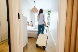 Une femme entrant dans une chambre avec une valise &agrave; roulettes.
