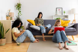 Trois &eacute;tudiantes &eacute;tudiant ensemble &agrave; la maison, assises confortablement sur le sol et le canap&eacute;, plong&eacute;es dans leurs devoirs universitaires. Concept d'amiti&eacute; f&eacute;minine et de jeunesse