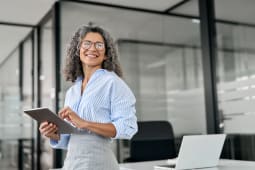 Femme d'affaires professionnelle mature souriante, directrice de banque plus &acirc;g&eacute;e, femme ex&eacute;cutive heureuse ou entrepreneuse &acirc;g&eacute;e tenant une tablette num&eacute;rique debout dans le bureau au travail, regardant ailleurs dans l'espace de copie.