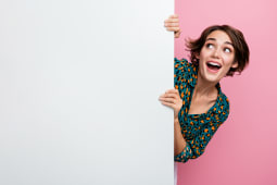 Portrait de femme ravie aux cheveux au carr&eacute; portant une blouse imprim&eacute;e tenant un mur blanc regardant l'offre d'un espace vide isol&eacute; sur fond rose