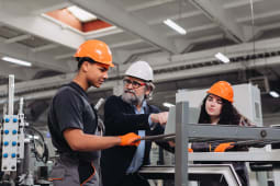 Ing&eacute;nieur exp&eacute;riment&eacute; guidant de jeunes apprentis en fabrication dans une usine