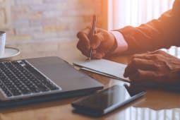 Un homme d'affaires �crit et signe un ch�que avec un ordinateur portable sur la table en bois d'un bureau moderne � domicile.