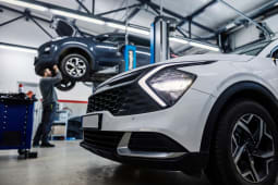 Une voiture au premier plan avec un m&eacute;canicien automobile r&eacute;parant une autre voiture en arri&egrave;re-plan.