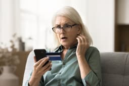 Femme &Atilde;g&eacute;e inqui&egrave;te et surprise en lunettes regardant un smartphone et une carte de cr&eacute;dit, rencontrant des probl&egrave;mes financiers, mauvais service bancaire en ligne, d&eacute;couvrant des d&eacute;penses excessives, risque de faillite