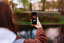 Une femme tient un smartphone affichant un message Pas de Signal tout en se tenant dans un parc pr&egrave;s de l'eau. L'image repr&eacute;sente une panne de r&eacute;seau cellulaire, une mauvaise connexion ou une perte de donn&eacute;es.