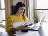 Une femme regarde son ordinateur et des documents.