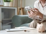 Quelqu'un tenant un téléphone portable à côté d'une calculatrice et d'une tirelire.