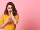 femme jeune, heureuse et surprise, belle à regarder, utilise un téléphone portable sur un fond rose avec de l'espace pour du texte.