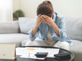 Une femme regarde des documents en se prenant la t&ecirc;te dans les mains.