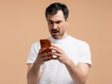 Un homme l'air surpris en regardant son t&eacute;l&eacute;phone.
