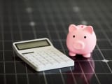 Gros plan d'une calculatrice blanche et d'une tirelire rose sur un panneau solaire photovolta&iuml;que.