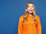 Jeune femme caucasienne choqu&eacute;e, surprise, excit&eacute;e et heureuse, elle porte un pull jaune d&eacute;contract&eacute; regardant de c&ocirc;t&eacute; sur une maquette d'espace de travail isol&eacute;e sur un fond bleu uni en studio. Concept de style de vie.