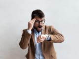 Jeune homme d'affaires en costume avec des lunettes avec une expression faciale choqu&eacute;e regardant sa montre parce qu'il est en retard. Concept de gestion du temps.