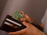 Gros plan des mains d'une personne tenant un portefeuille en cuir marron rempli de billets en euros et de cartes de cr&eacute;dit