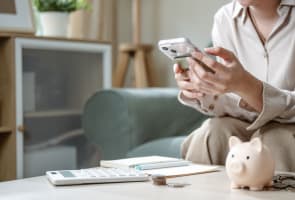 Quelqu'un tenant un t�l�phone portable � c�t� d'une calculatrice et d'une tirelire.