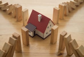 Maison entour�e de blocs de bois tombant comme des dominos.