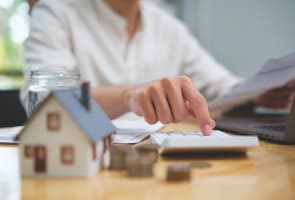 Personne calcule des finances immobili�res avec maison miniature et pi�ces.