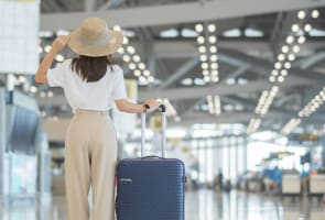 Une jeune femme tenant la poign�e de sa valise et v�rifiant l'heure de son voldans un a�roport.