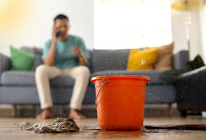 Un seau recueille de l?eau qui fuit du plafond, avec en fond, un homme au t�l�phone.