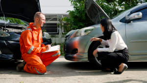 Une femme et un homme accroupis pr�s d'une voiture en panne.