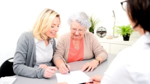 Une femme âgée signe un document à côté d'une autre femme plus jeune.