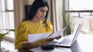 Une femme regarde son ordinateur et des documents.