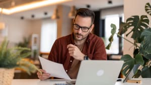 Un homme regarde son ordinateur et des documents.