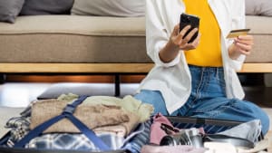 Une personne regarde sa carte bancaire, près d'une valise.