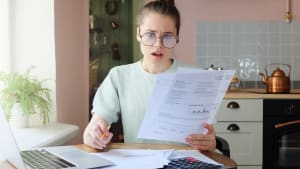 Une femme regarde son ordinateur et des documents l'air surpris.