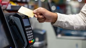 Une main tenant une carte de crédit au-dessus d'un terminal de paiement lors d'un achat dans un magasin. Concept de paiement sans contact.