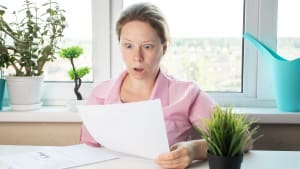 Une femme choque regardant une lettre, examinant des papiers avec des documents bancaires.