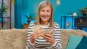 Heureuse femme caucasienne mature compte de l'argent en euros en espces dans ses mains aprs avoir gagn un bonus de loterie ou reu un cadeau. La grand-mre sourit largement assise sur le canap de sa maison, clbrant sa victoire financire salariale.