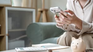 Quelqu'un tenant un tlphone portable  ct d'une calculatrice et d'une tirelire.