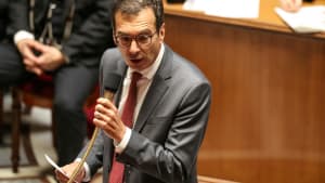 Homme en costume parlant au micro dans une salle formelle. Farandou