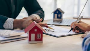 Signature de documents immobiliers avec des maisons miniatures.