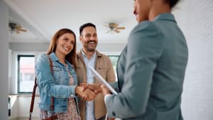 Une femme et un homme serrent la main d'un agent immobilier.