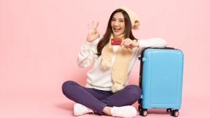 Une femme souriante  ct d'une valise avec une carte bancaire.
