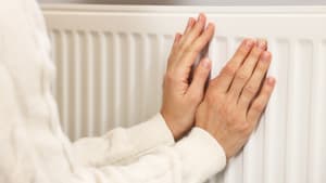 Une femme se réchauffant les mains près du radiateur.