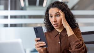 Une jeune femme dans un bureau lisant un message sur son smartphone et r�agissant avec surprise.