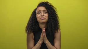 Jeune femme hispanique frottant ses doigts en studio sur un mur jaune avec un regard inquiet ; un appel dsespr  l'aide.