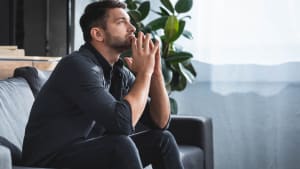 vue de ct d'un bel homme pensif assis sur le canap et regardant