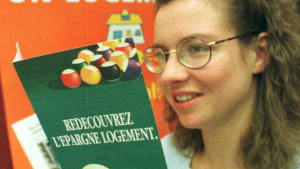 Femme souriante tenant une brochure sur l'épargne logement.