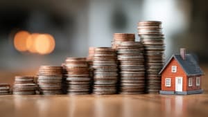 Piles de pices avec petite maison rouge sur table.